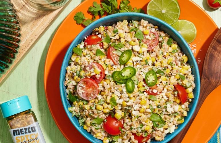 Fresh grain salad in blue bowl with MEZCO SPICE BLEND, on pastel green-orange background.