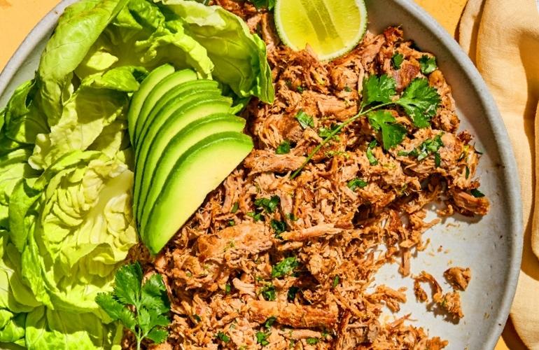 Shredded meat meal with avocado, cheese, sauce, and lime under warm sunlight.