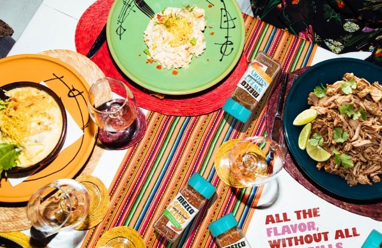 Mexican dinner spread with dishes, wine, colorful tablecloth, MEZCO bottles, and flavor slogan.